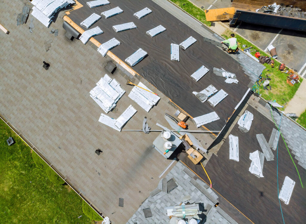 Top-down, aerial view of roofing contractors repairing damaged shingles on a roof.